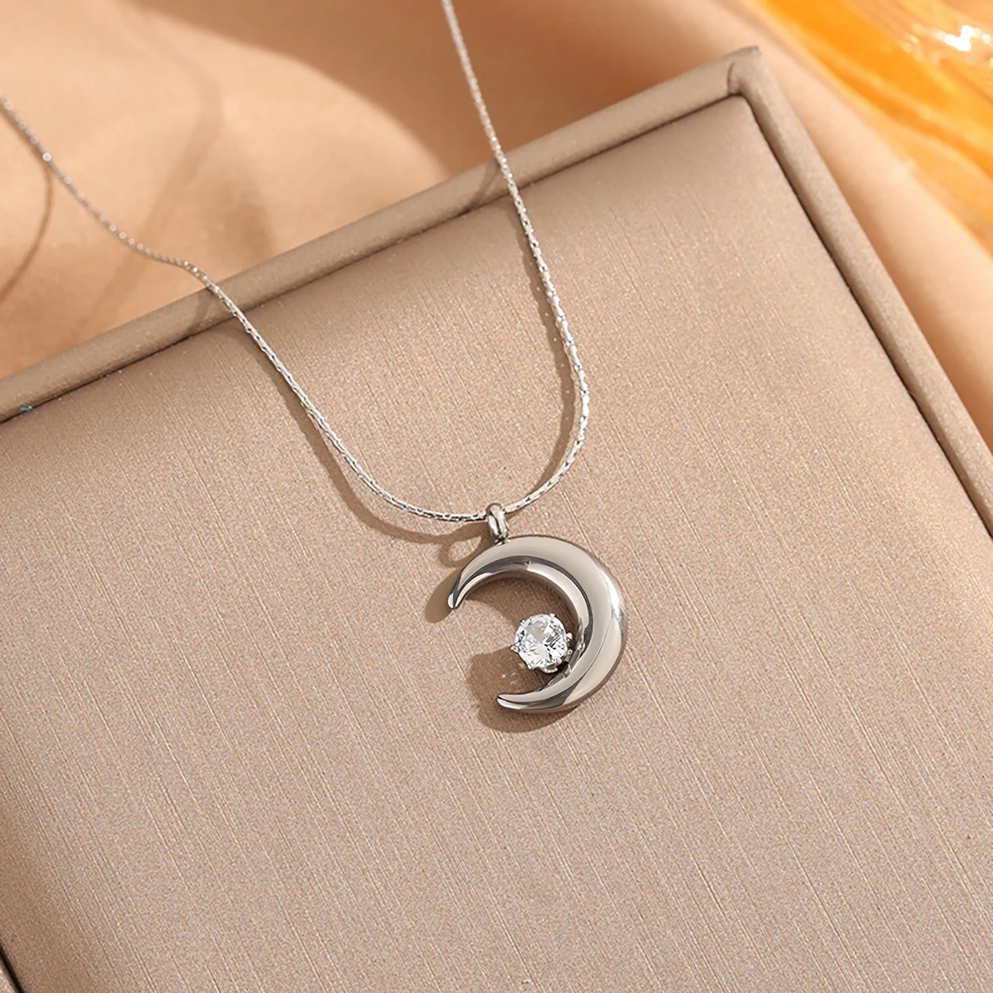 Silver necklace with a crescent moon pendant on a beige surface