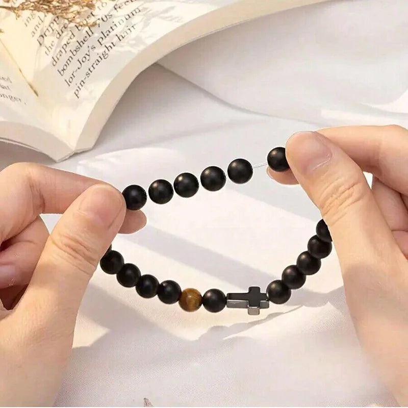 Hands stretching elastic natural stone cross bracelet showing comfortable adjustable fit