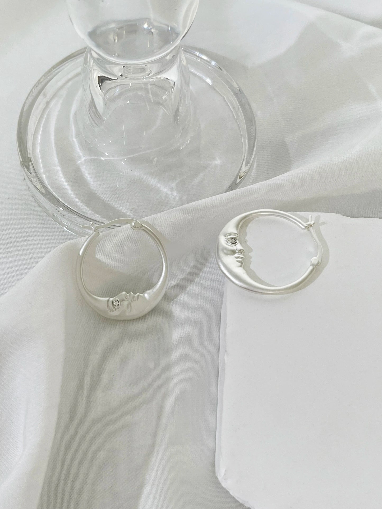 Two silver rings on a white fabric surface with a glass object in the background.