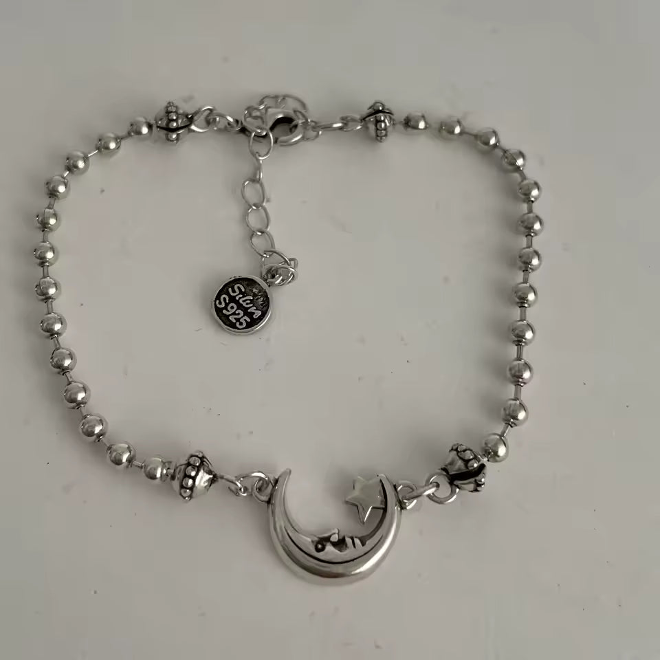 Silver bracelet with a moon and star charm on a light gray background