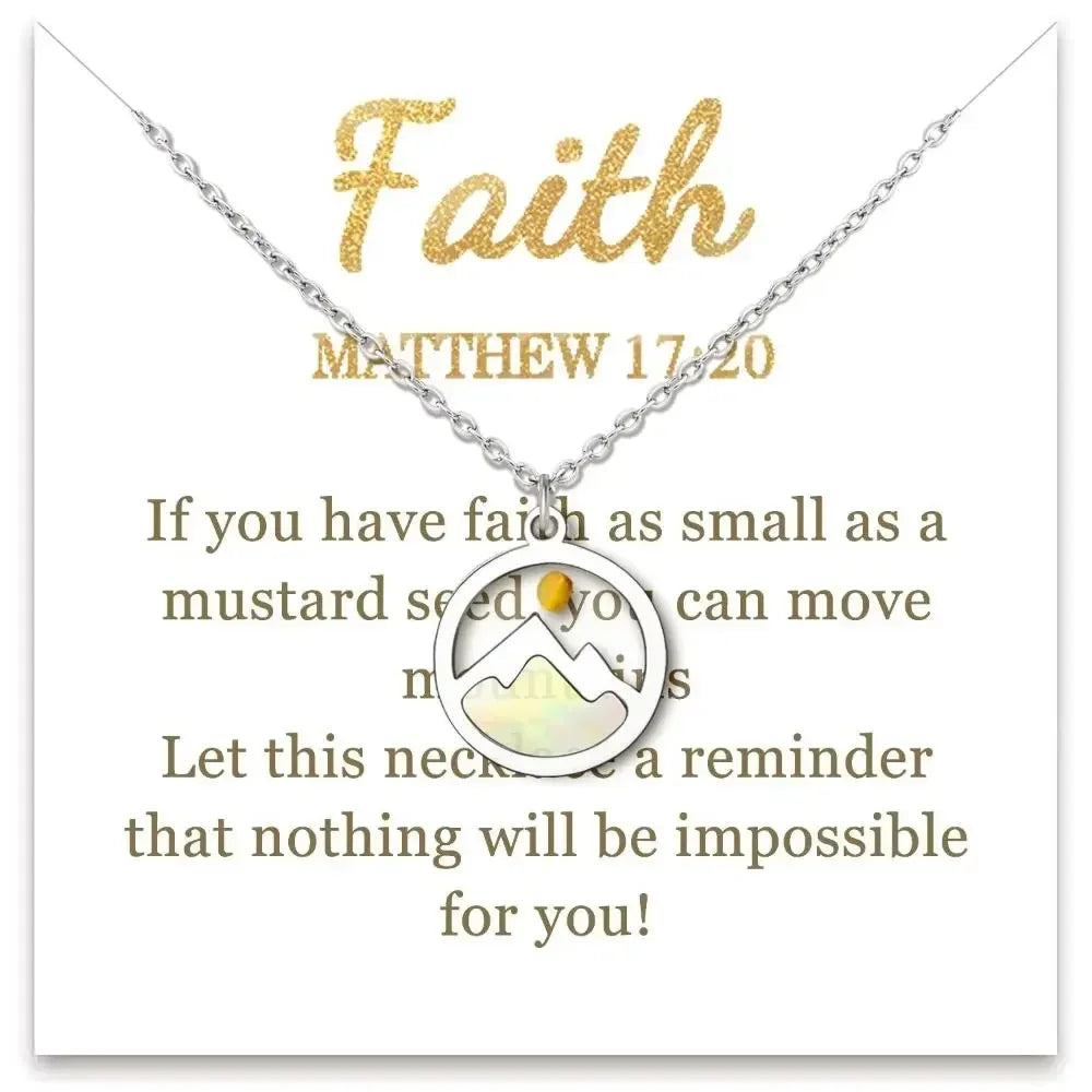 A silver chain necklace with a circular pendant featuring a white mountain and a small amber-yellow sun, displayed on a white card with gold text reading 'Faith' and 'MATTHEW 17:20'.