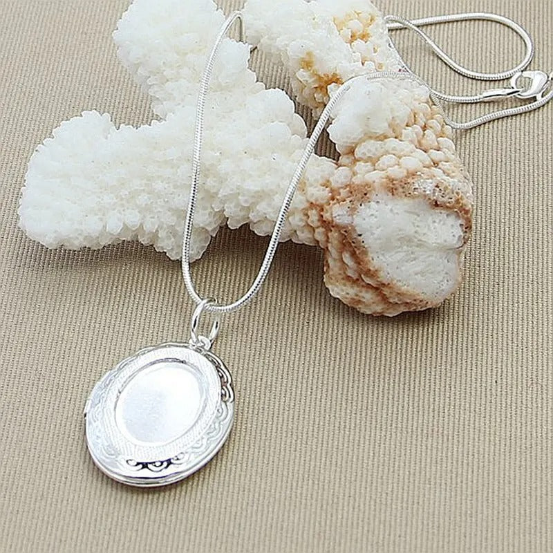 Silver locket necklace on a beige surface with decorative stones