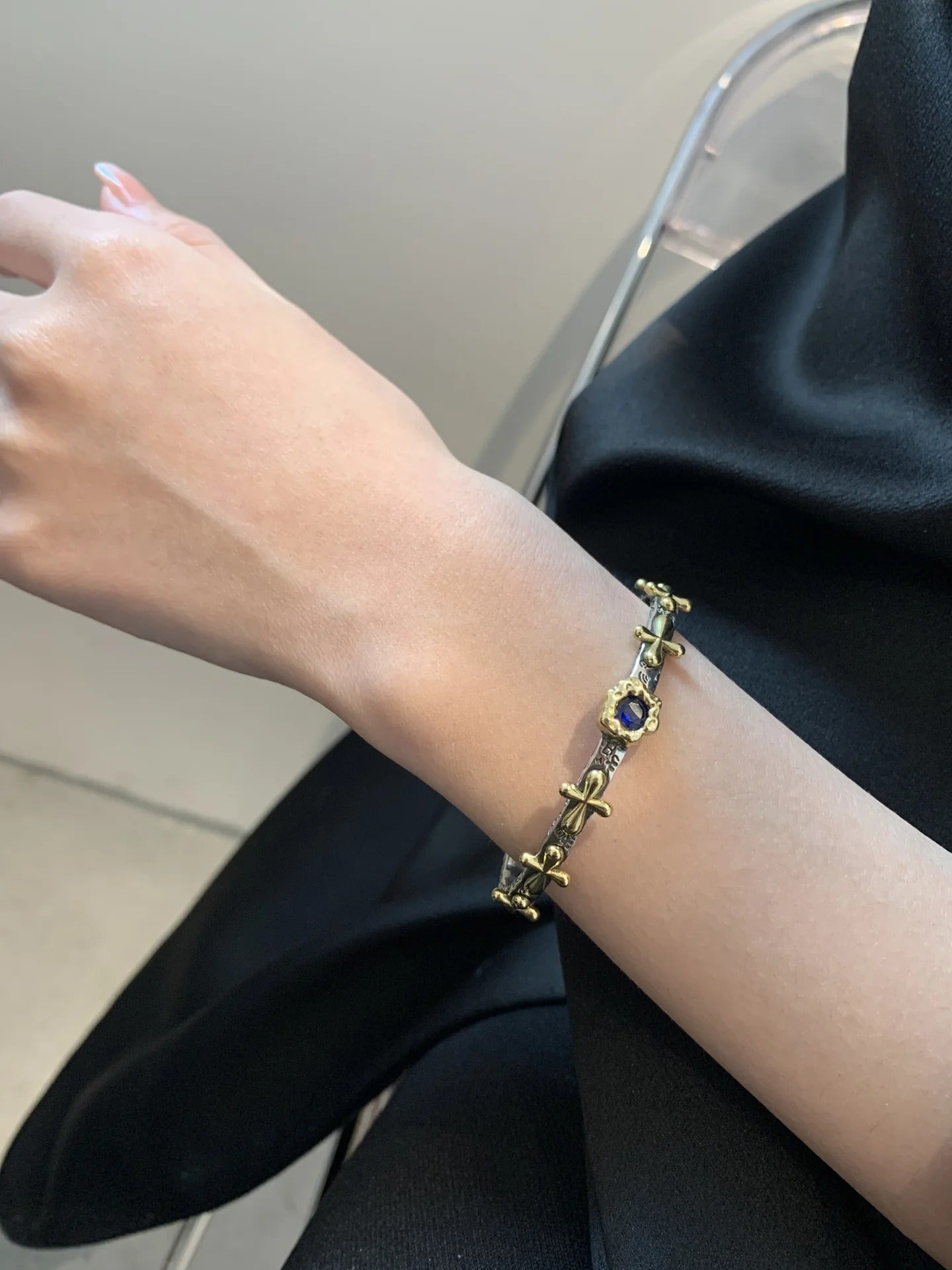 Gold bracelet with a blue gemstone on a person's wrist against a black background