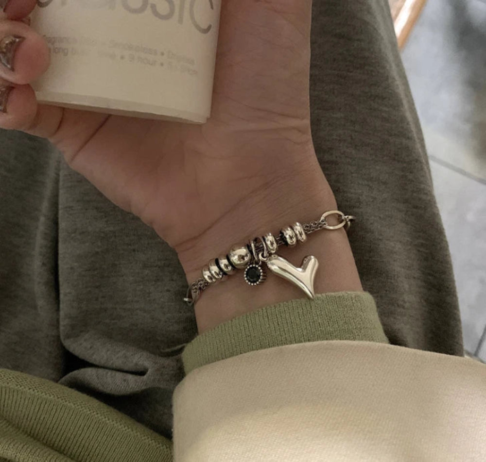 Hand wearing a bracelet with charms, holding a product, against a neutral background