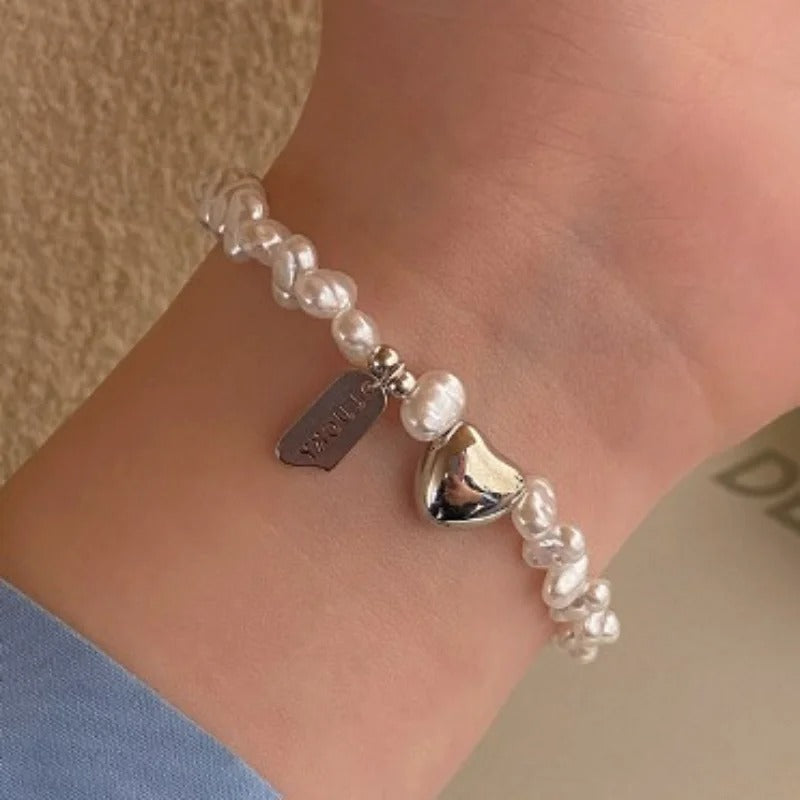Pearl bracelet with a heart charm on a wrist against a neutral background