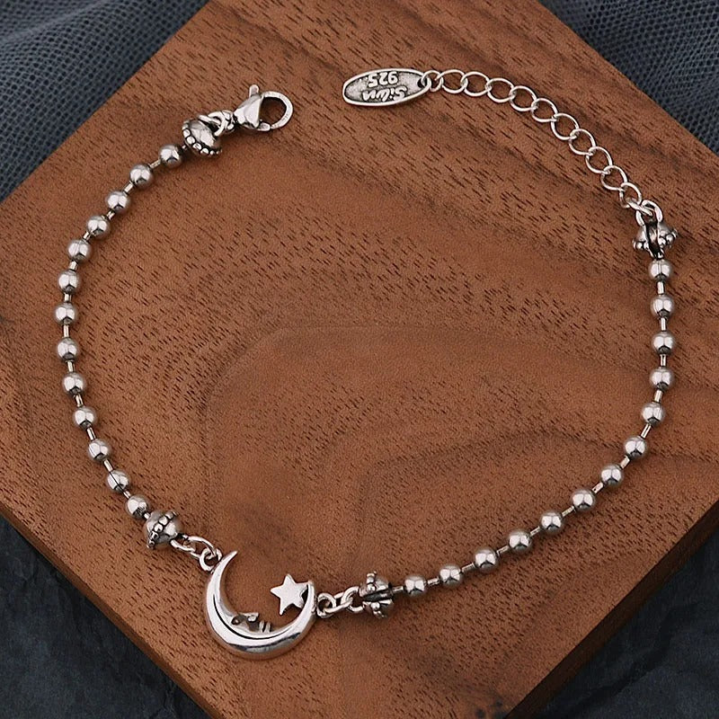 Silver bracelet with moon and star charm on a wooden surface