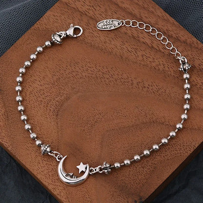 Silver bracelet with moon and star charm on a wooden surface