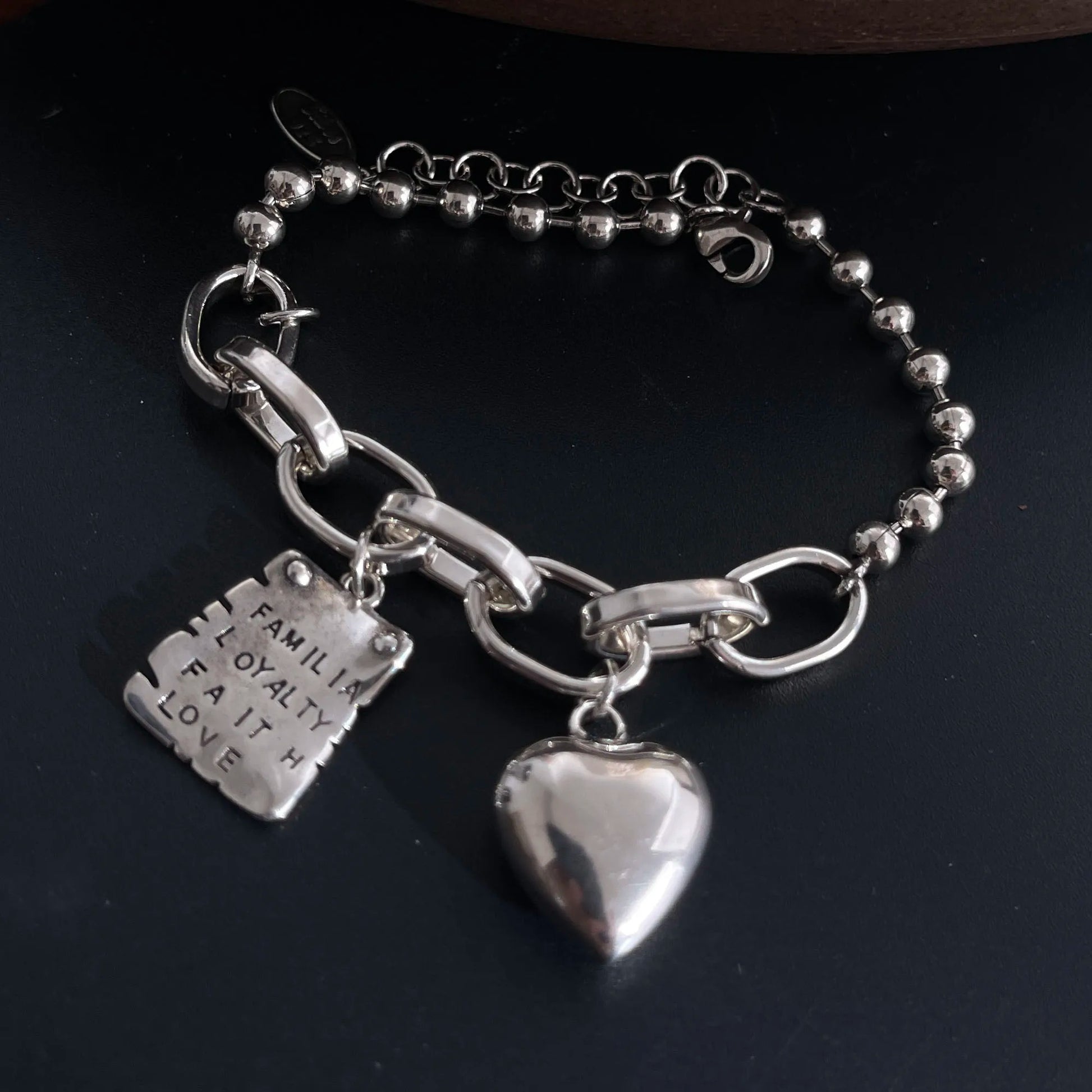 Silver bracelet with heart charm and engraved tag on a dark background