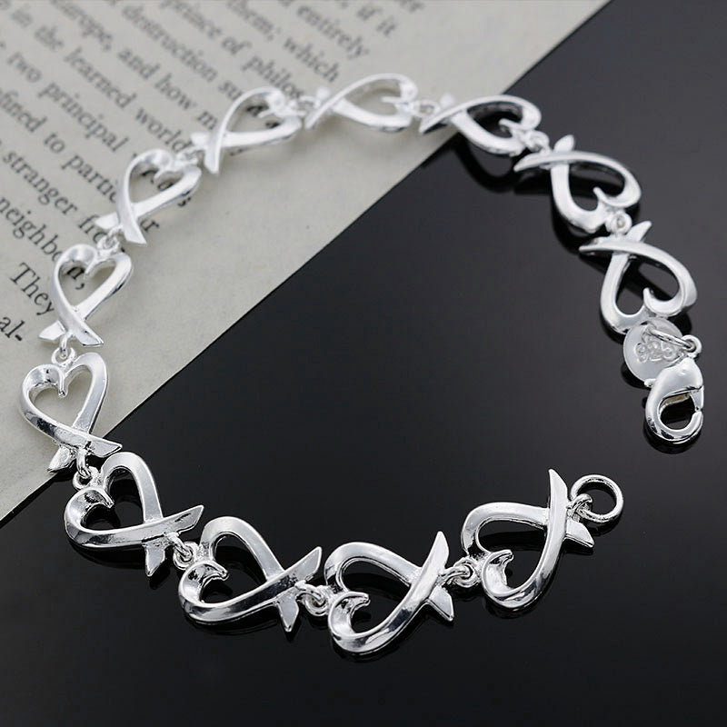 Silver bracelet with heart and infinity designs on a black and white background