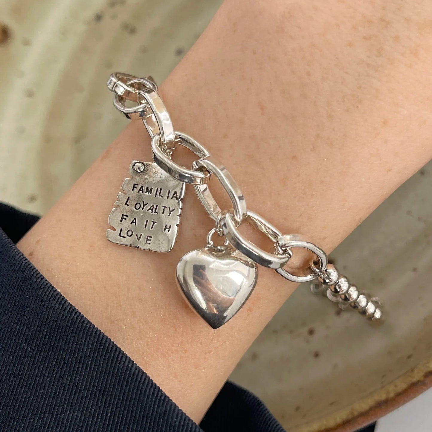 Silver bracelet with heart charm and engraved tag on wrist