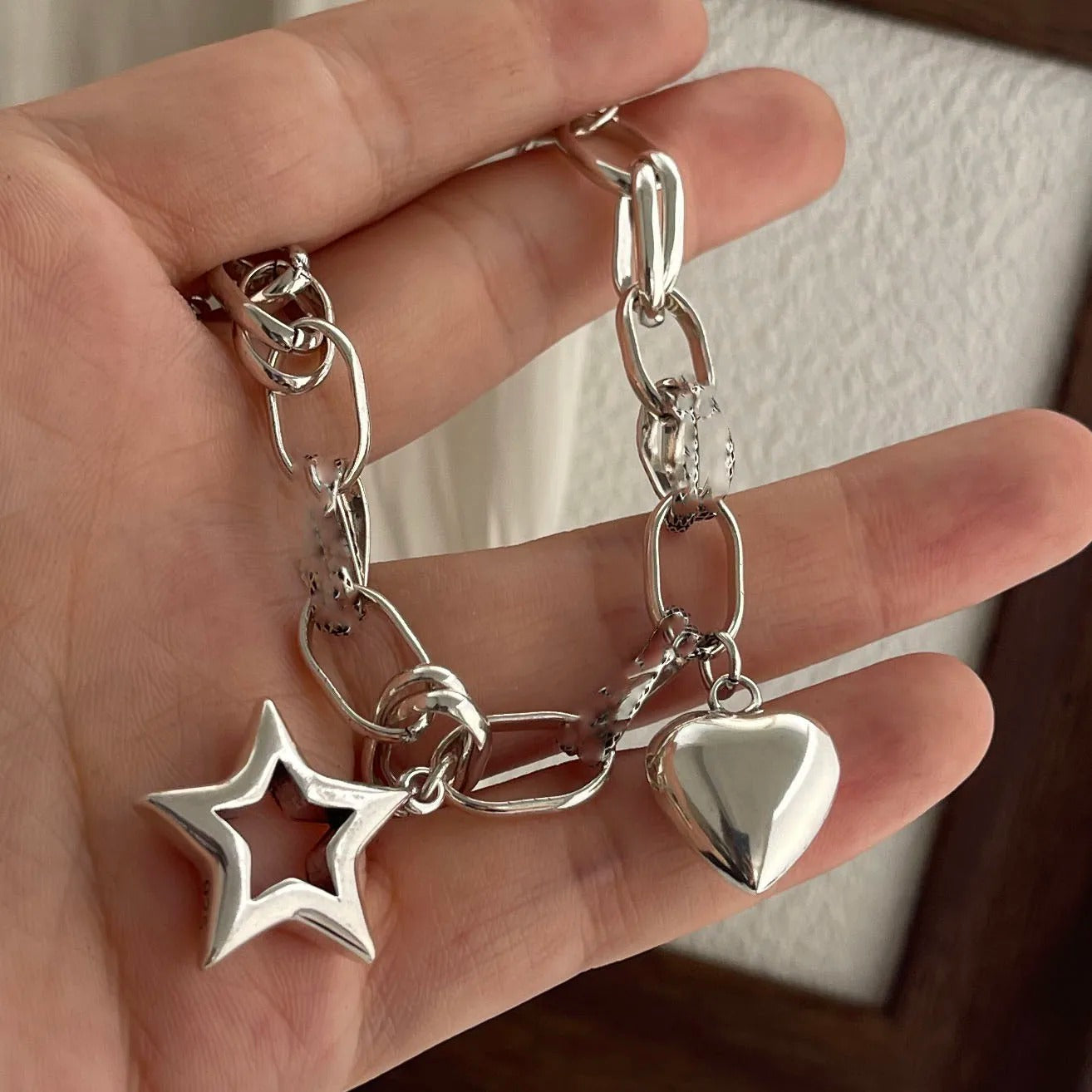 Silver bracelet with star and heart charms held in a hand against a neutral background