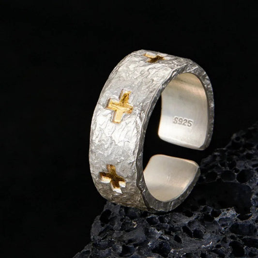 Silver ring with gold crosses on a dark textured surface