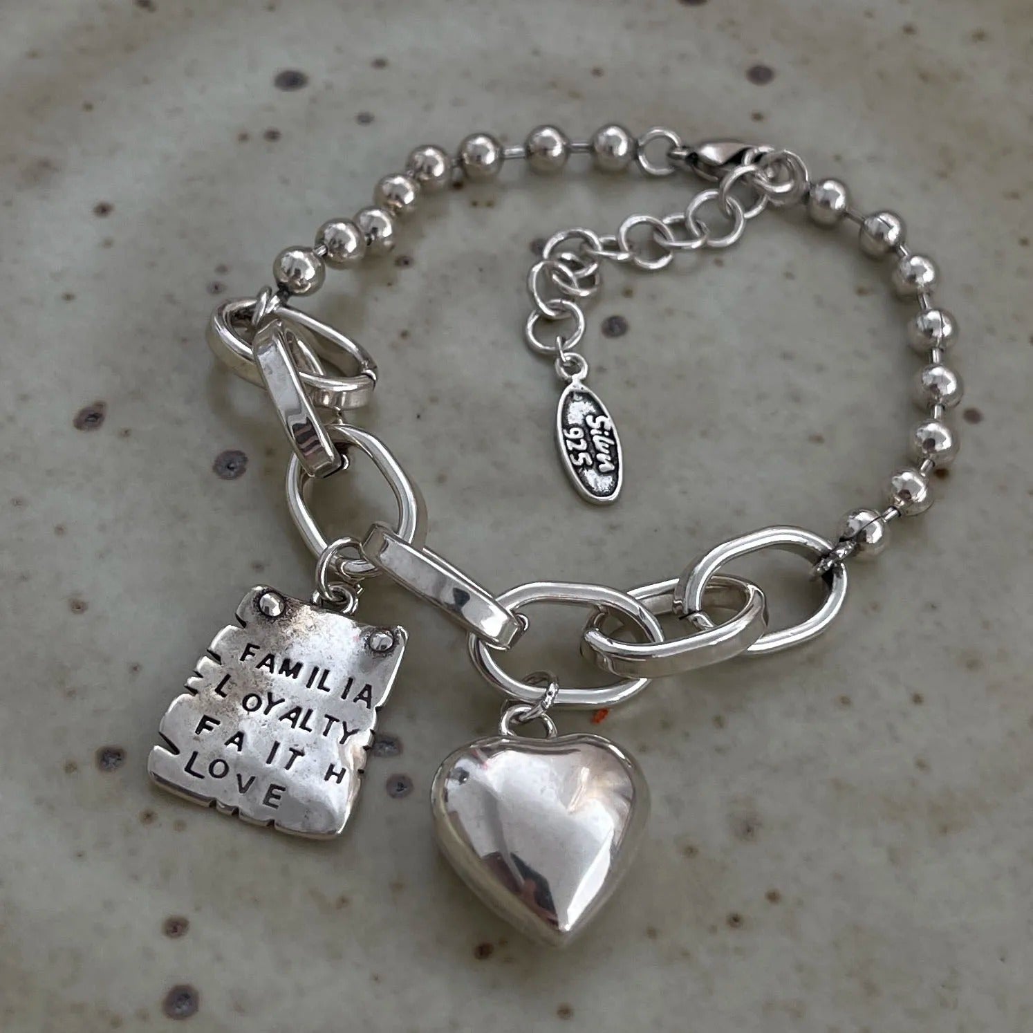 Silver bracelet with heart and tag charms on a textured surface