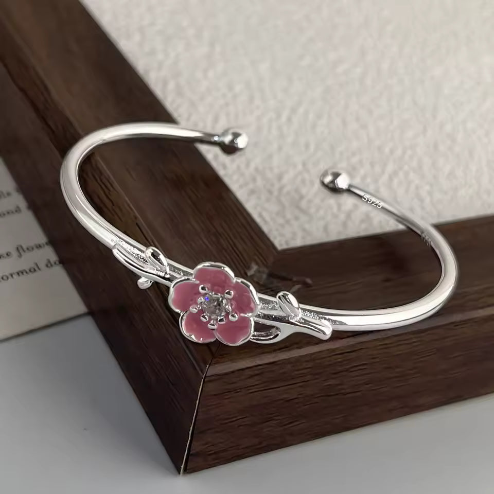 Silver bracelet with a pink flower charm on a wooden surface