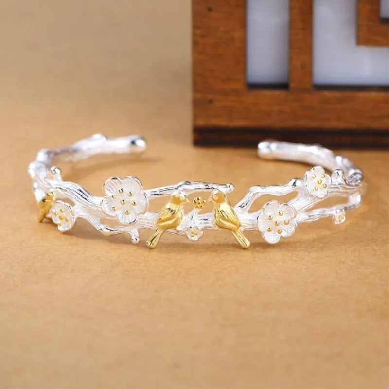 Silver bracelet with floral and bird designs on a beige surface