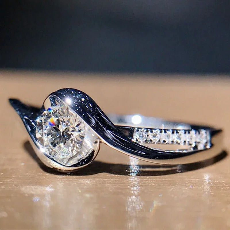Diamond ring with a large central gemstone and smaller stones on a reflective surface