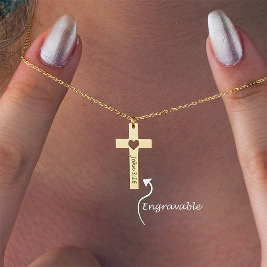 Gold cross necklace with heart detail held by a hand against a neutral background