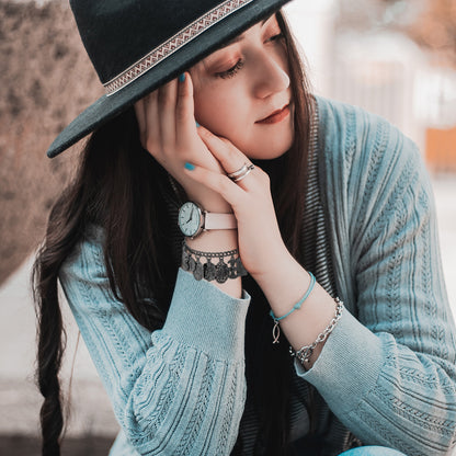 Woman wearing a black hat and light blue sweater with jewelry, sitting outdoors.