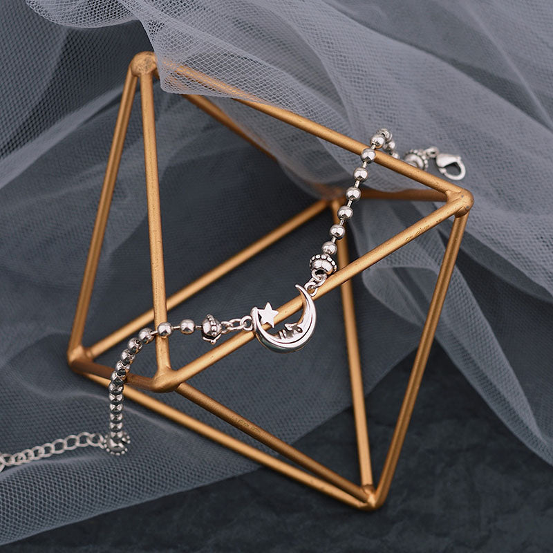 Bracelet with star and moon charm on a gold geometric stand against a gray background