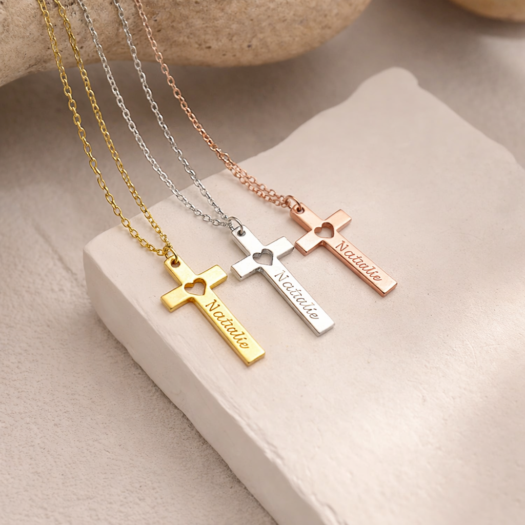 Three cross-shaped necklaces in gold, silver, and rose gold on a beige surface.