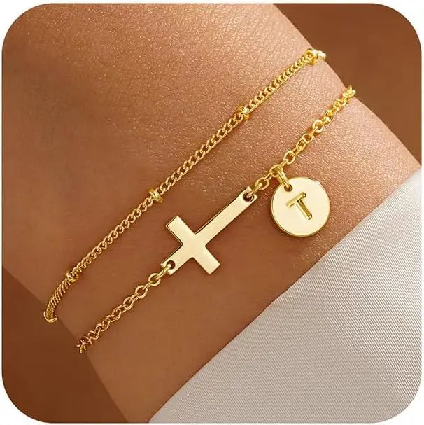 Gold bracelet with cross and circular charm on a wrist against a brown background