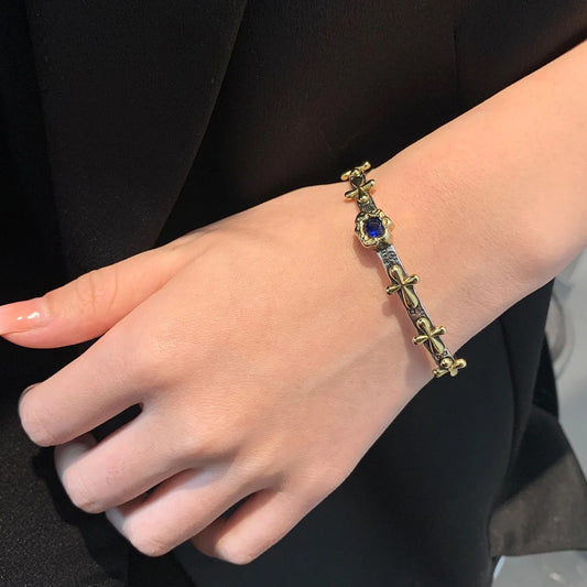 Gold bracelet with a blue gemstone on a person's wrist against a black background