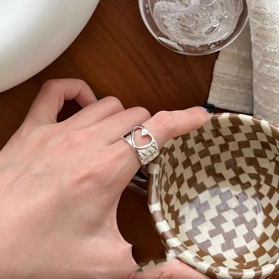 Hand wearing a silver ring holding a woven basket on a wooden surface.