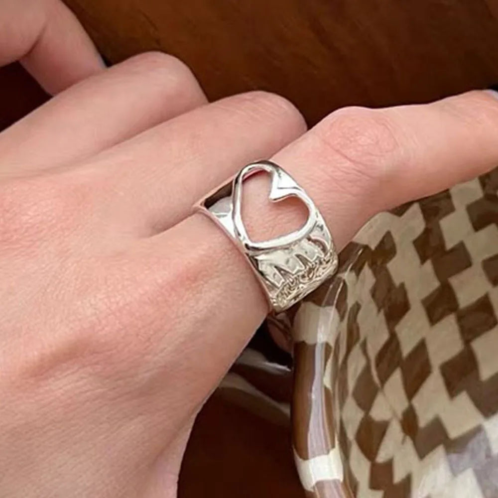 Hand wearing a silver ring with a heart design on a checkered fabric background