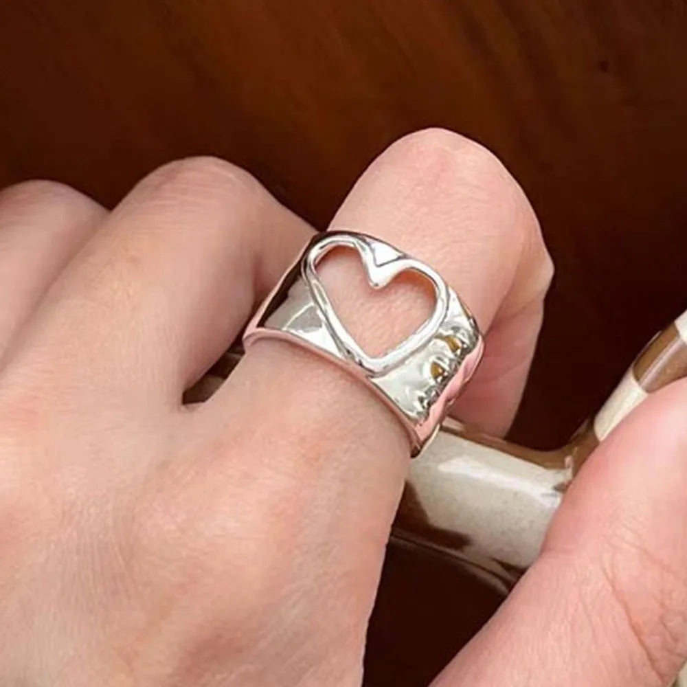 Silver ring with heart design on a finger against a wooden background