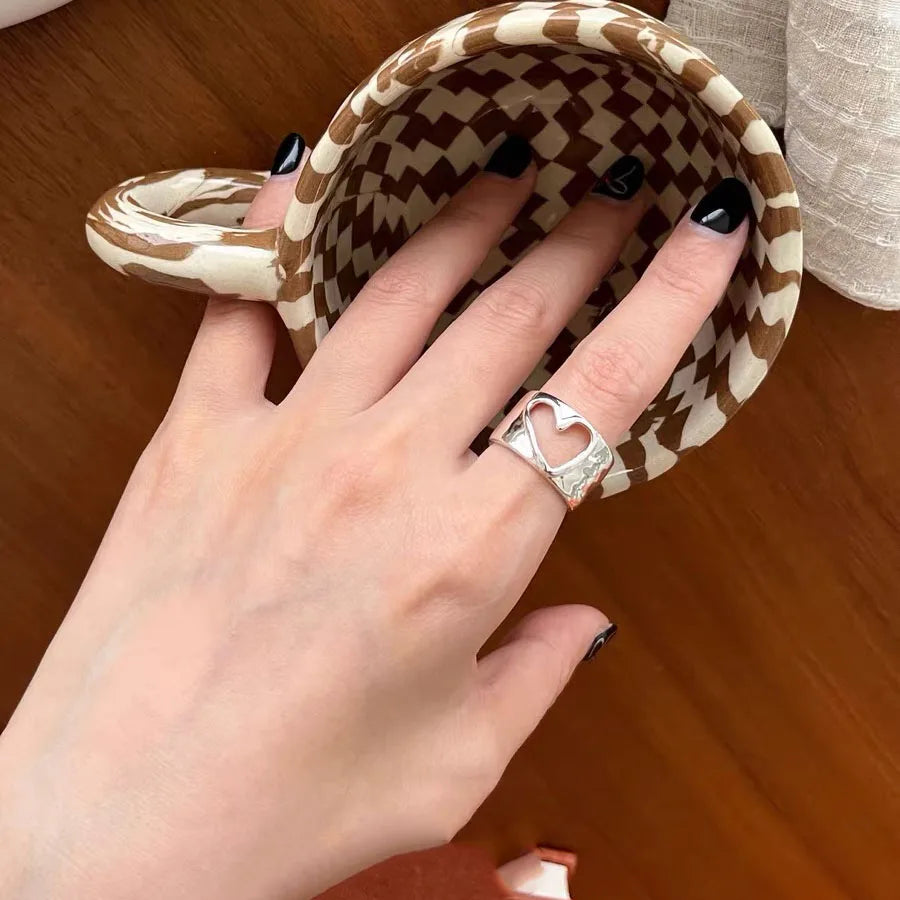Hand wearing a silver ring with a heart design on a checkered surface.