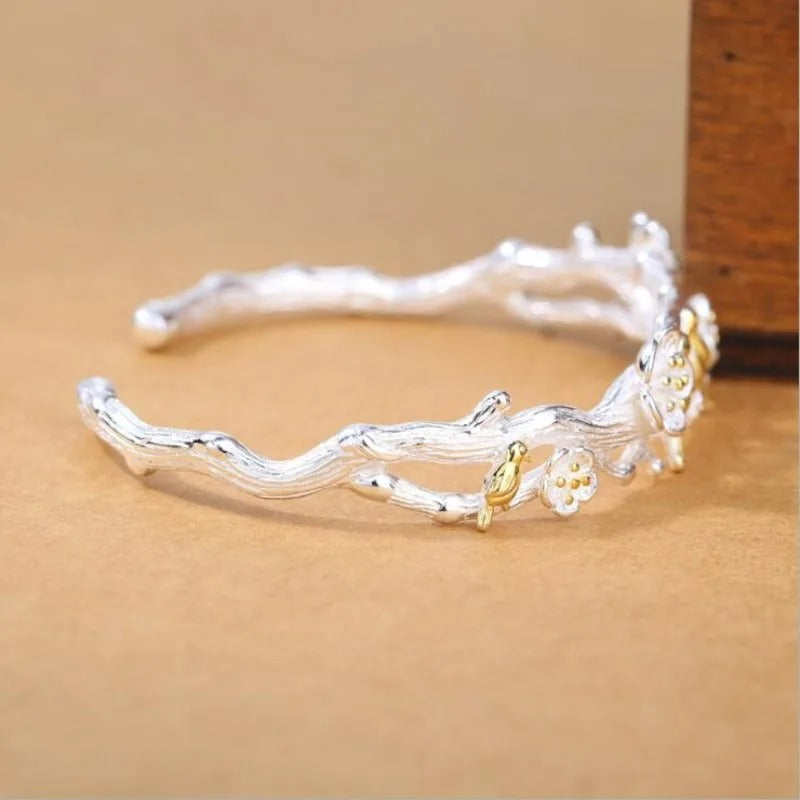 Silver branch-like bracelet with gold accents on a beige background