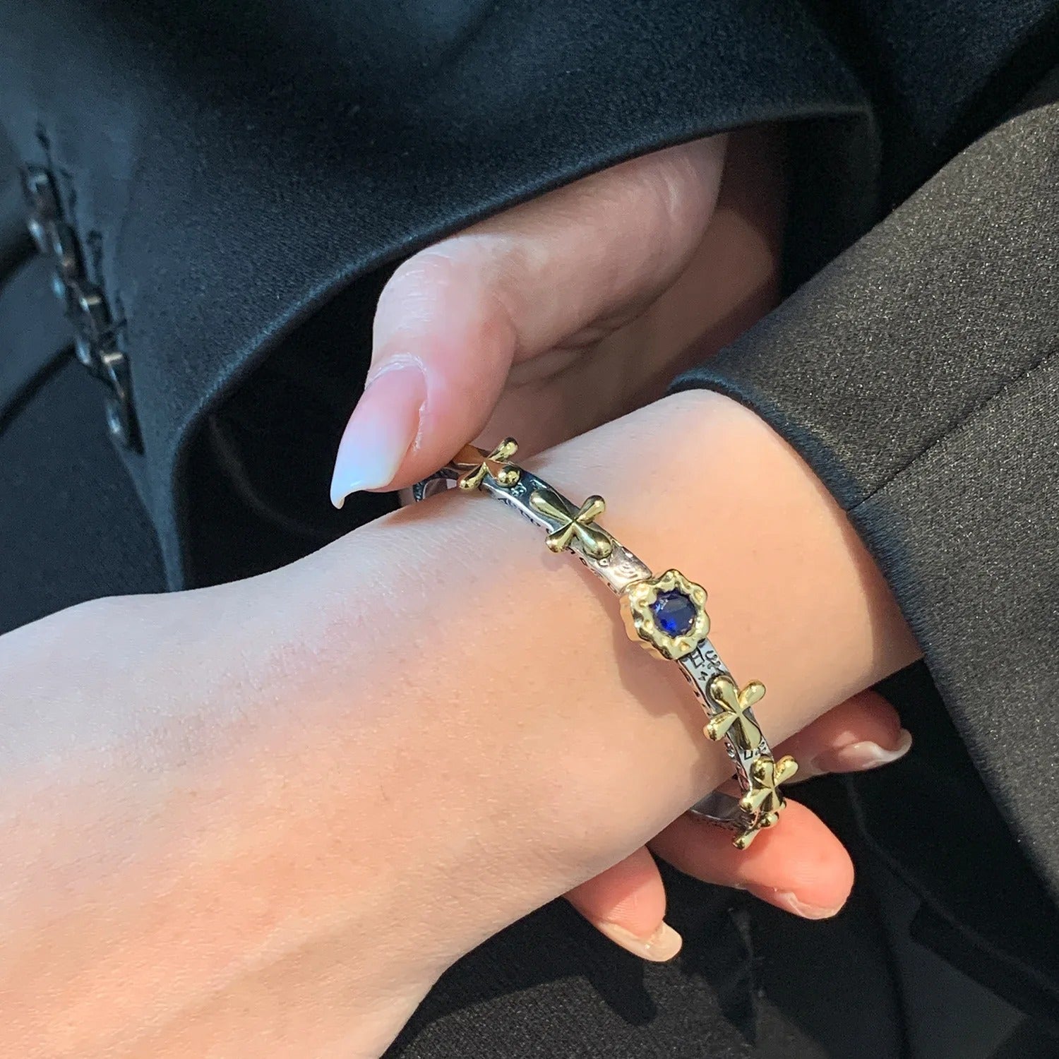Close-up of a hand wearing a gold bracelet with blue stone on a dark background