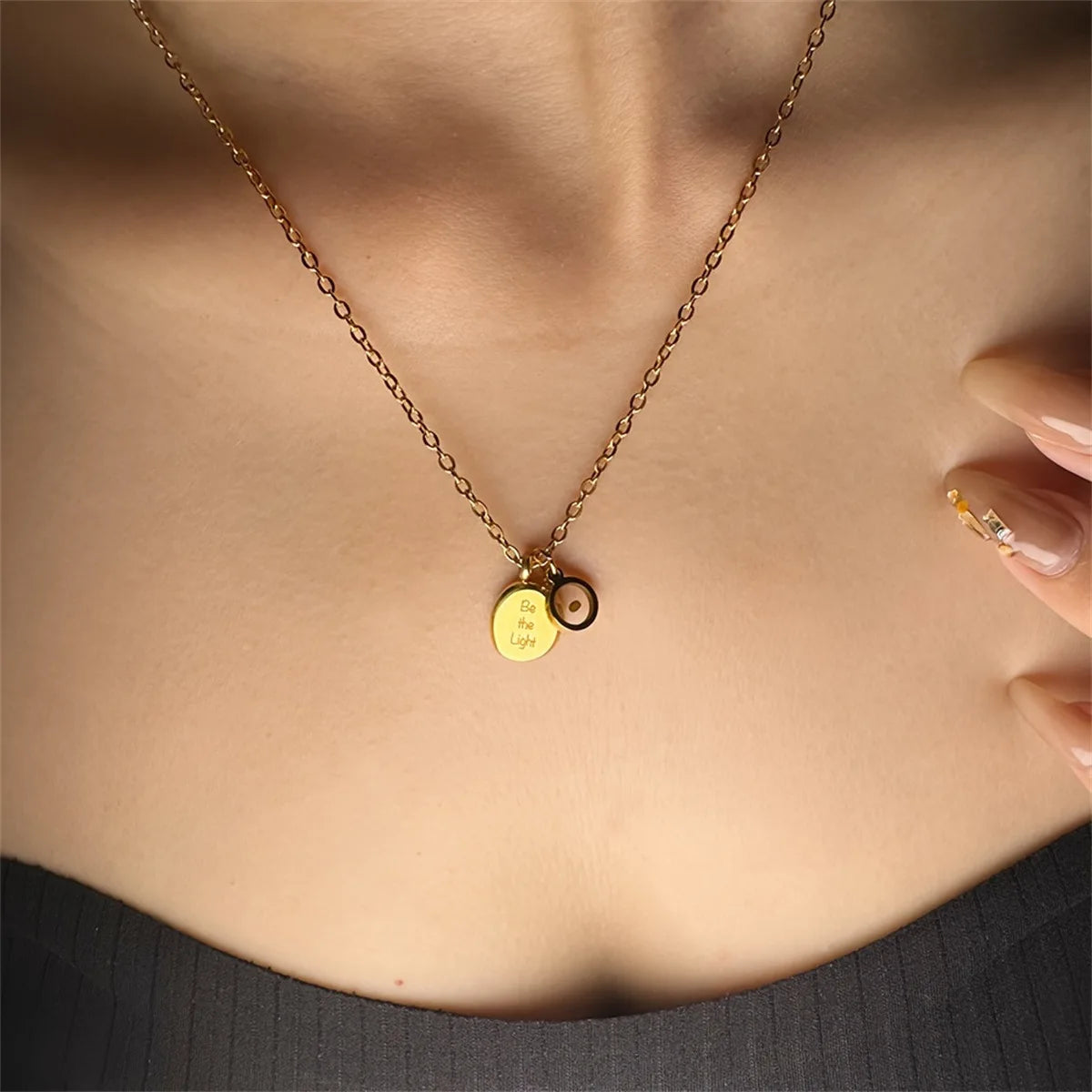 Gold necklace with round pendants on a person wearing a dark top.