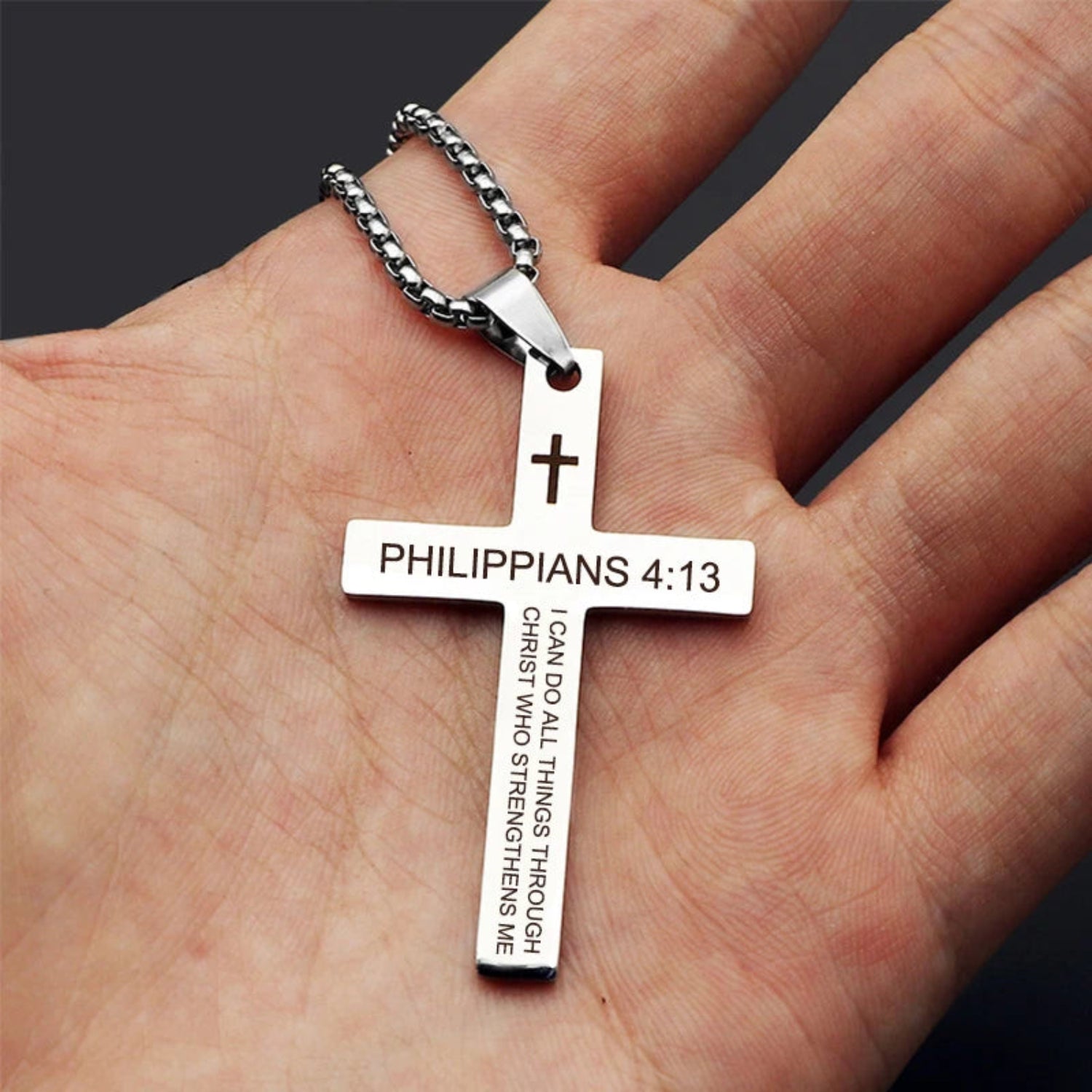 Silver cross pendant with 'Philippians 4:13' text on a hand