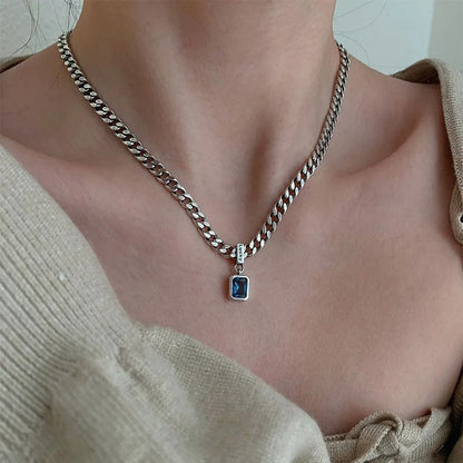 Necklace with a blue pendant worn by a person in a beige sweater.