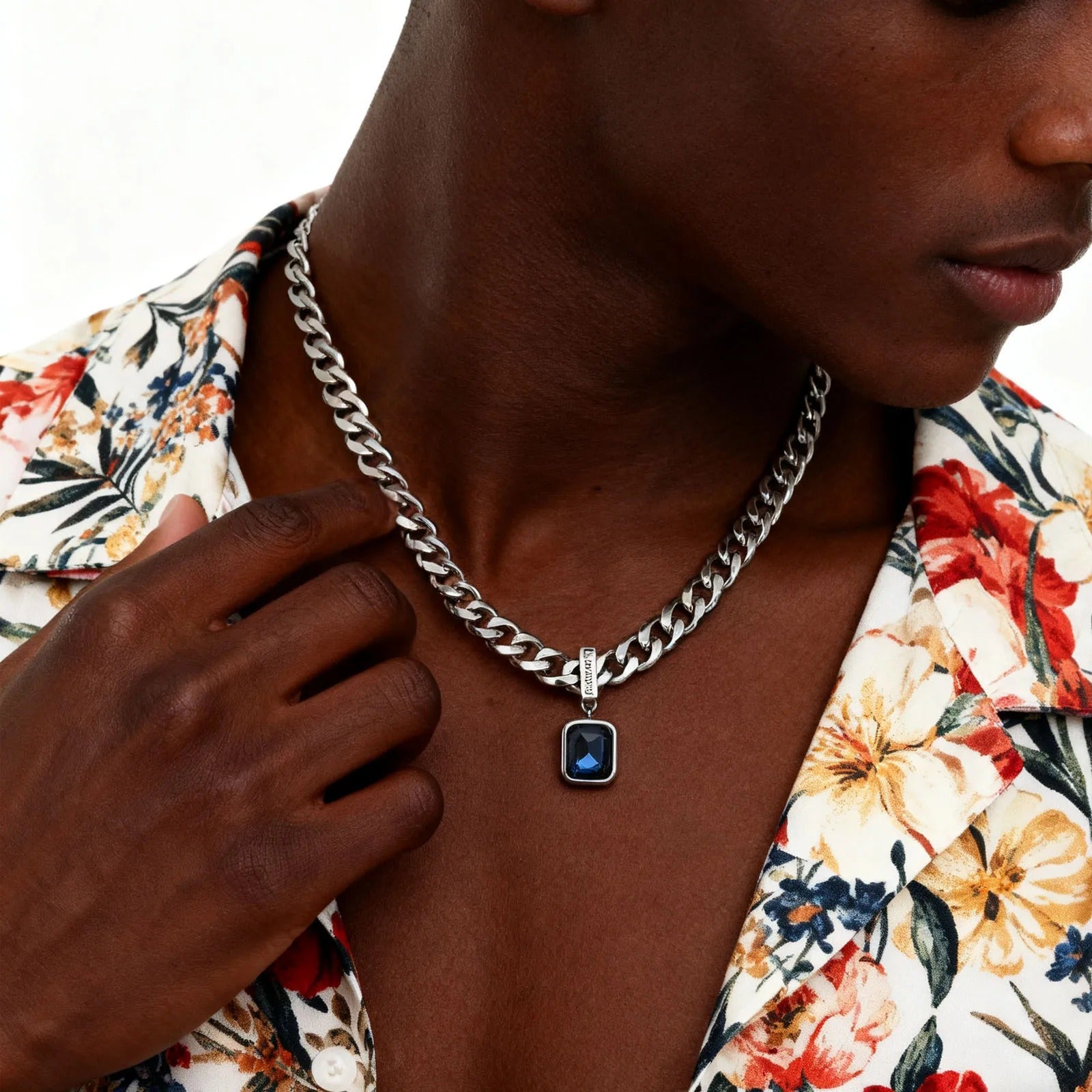 Person wearing a floral shirt and silver chain necklace with a blue pendant.