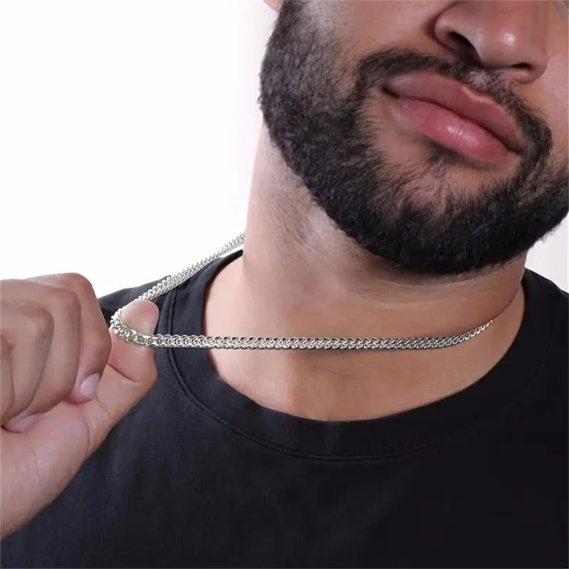 Man wearing a silver chain necklace against a plain background