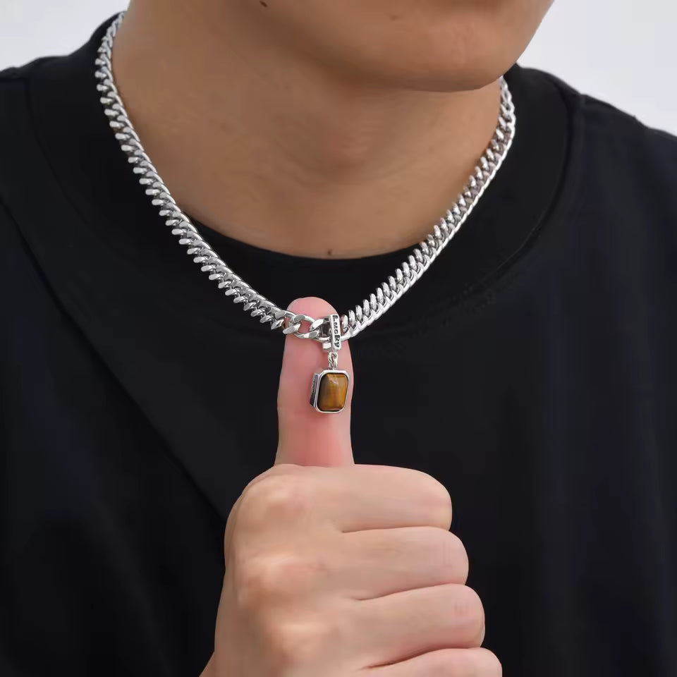 Person wearing a silver chain necklace with a brown stone pendant, pointing to the necklace.