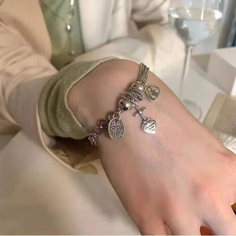 Close-up of a wrist wearing a silver bracelet with charms, blurred indoor background