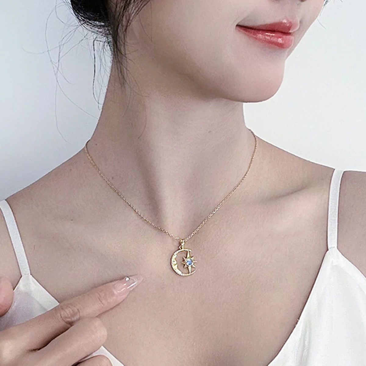 Gold necklace with a moon and star pendant worn by a person in a white top.