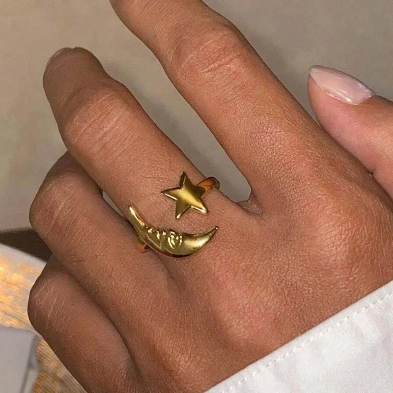 Gold ring with star and moon design on a finger against a neutral background