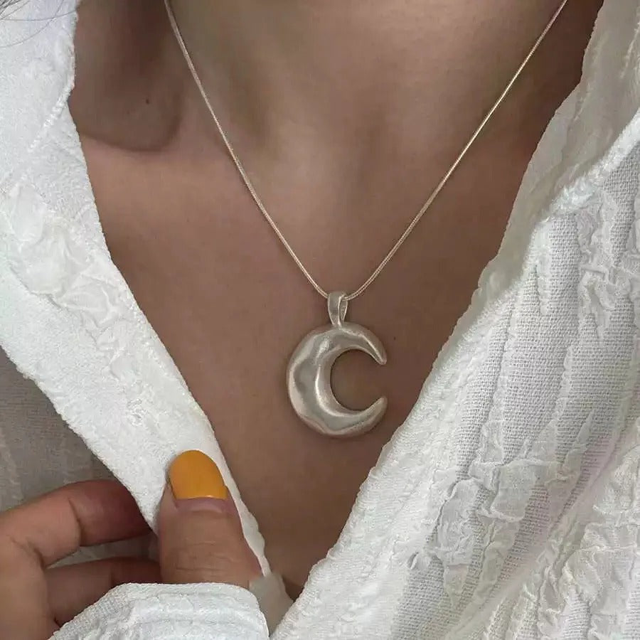 Silver moon-shaped pendant necklace on a person wearing a white textured garment.