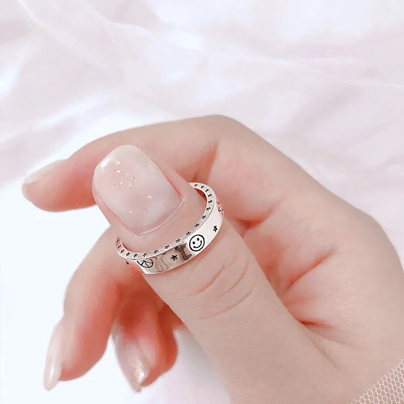 Hand wearing a silver ring with smiley face design on a light pink background