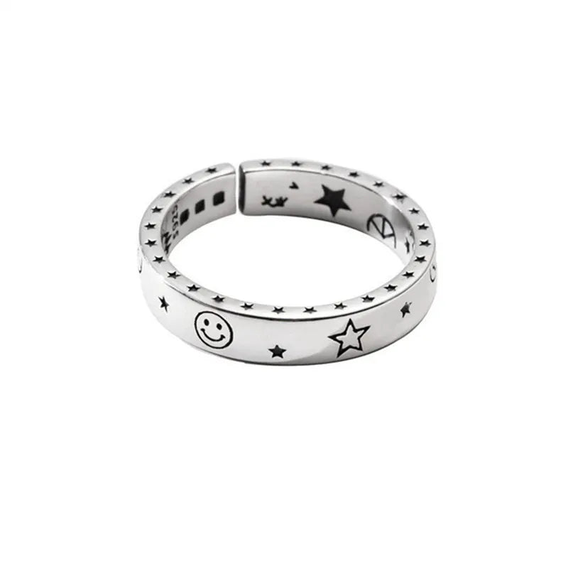 Silver ring with star and smiley face designs on a white background
