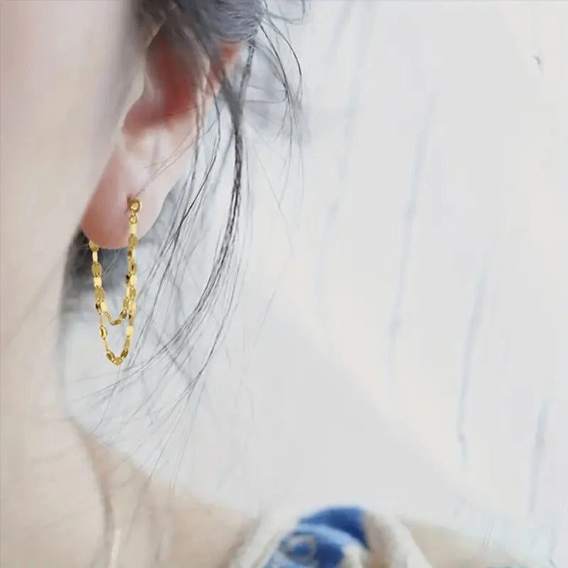 Gold chain earring worn by a person with a blurred background