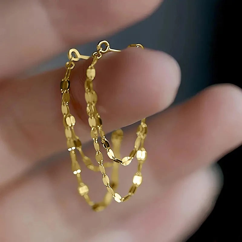 Gold hoop earrings being held between fingers against a blurred background