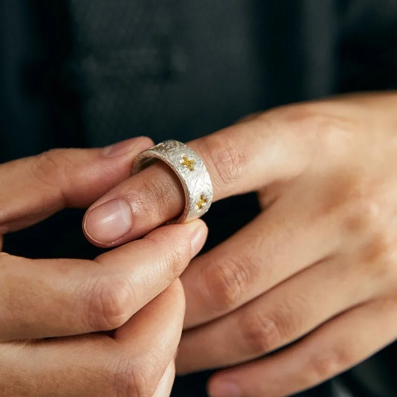 Close-up of a hand wearing a silver ring with gold crosses.
