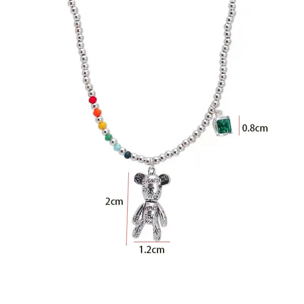 Silver beaded necklace with a teddy bear pendant, a small square green gem charm, and a short strand of multicolor beads, shown with dimension labels on a white background.