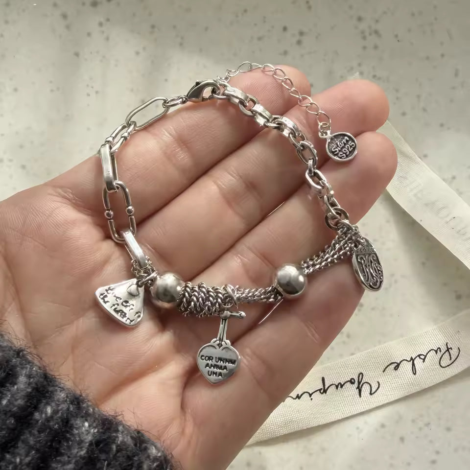 Silver bracelet with charms held in a hand on a textured surface