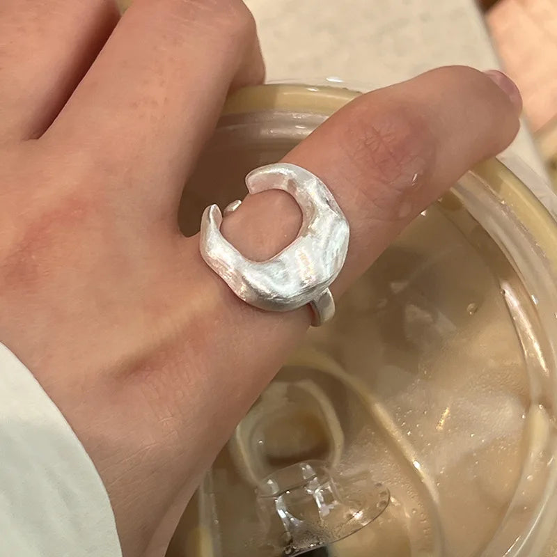 Hand wearing a silver ring with a textured design, holding a clear container.